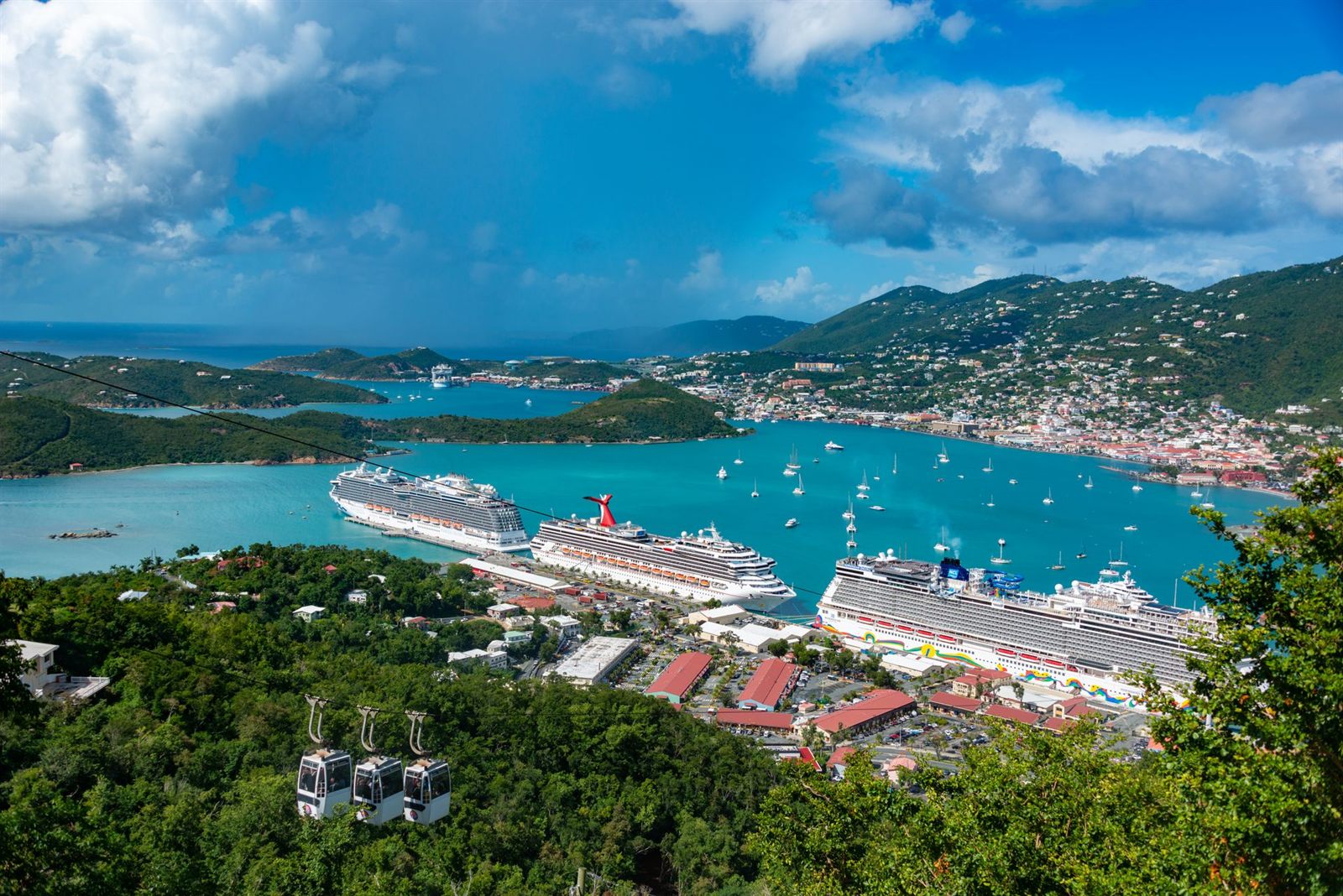 Cruise ships docked in a Caribbean harbor below green hills